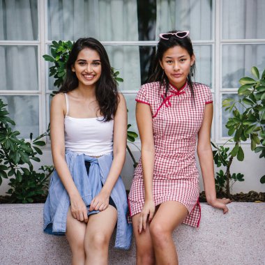 farklı etnik yapı birlikte dışarı asılı iki genç kadın arkadaşlar. Bir Çinli bir kadını bir cheongsam ve diğer bir Hint kadının modaya uygun bir kıyafet olduğunu