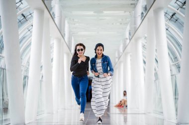 İki farklı arkadaş, iyi aydınlatılmış beyaz fütüristik bir üstgeçit köprüsünden kameraya doğru koşuyorlar. Biri Müslüman bir Orta Doğulu kadın, diğeri de Çinli..