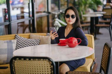 Bir açık havada açık havada oturan ve kırmızı bir çay seti çay sıcak bir fincan zevk genç, çekici, zarif ve güzel Asyalı kadın Portresi. 