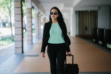 Genç bir Asyalı kadın bavulunu çekiyor. O çekici, zarif ve şık giyinmiş