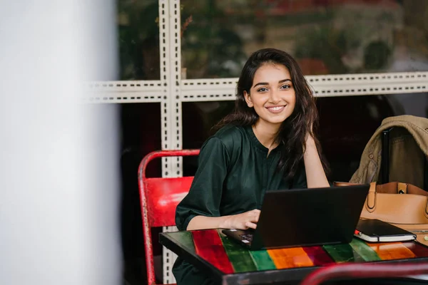 young university student (Indian Asian woman) is studying and working on her laptop computer at a table during the day