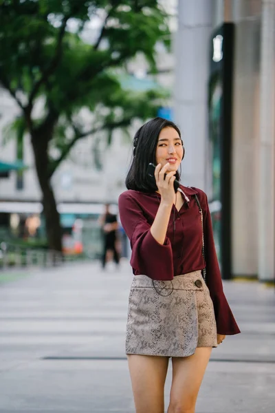 beautiful Korean woman in an elegant blouse and shorts dancing as she walks down a street in the city with her headphones on