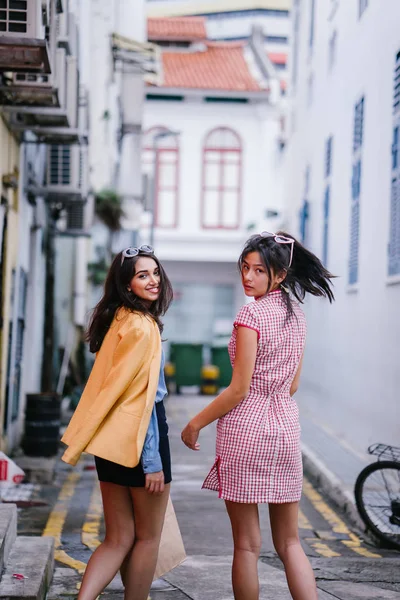 iki yakın arkadaş birlikte bir ara Sokaktan yürürken. Onlar birlikte mutlu bir şekilde yürürken onlar hem trendy retro giyim ve tutuşup giyiyorsun. Çince, diğer Hint biri