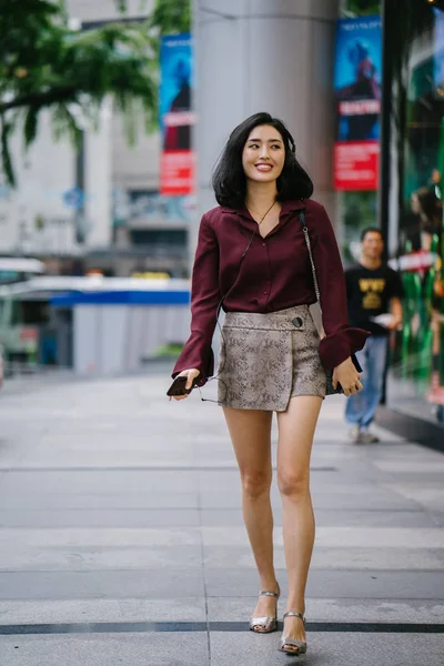 beautiful Korean woman in an elegant blouse and shorts dancing as she walks down a street in the city with her headphones on