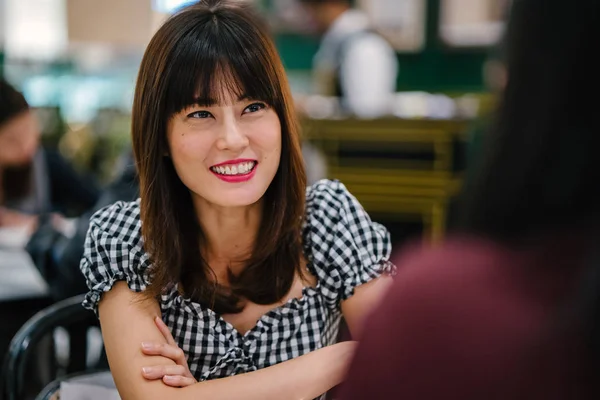 A Chinese Asian lady enjoys high tea with a good friend at a restaurant. She is beautiful, elegant and is smiling as she talks animatedly with her friend over cakes and tea on a weekend.