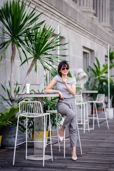 Açık havada şık bir yerde oturan bir emin, şık ve çekici orta yaşlı Çinli Asyalı kadın portresi. O bir pohpohlama gri kıyafeti giyiyor.