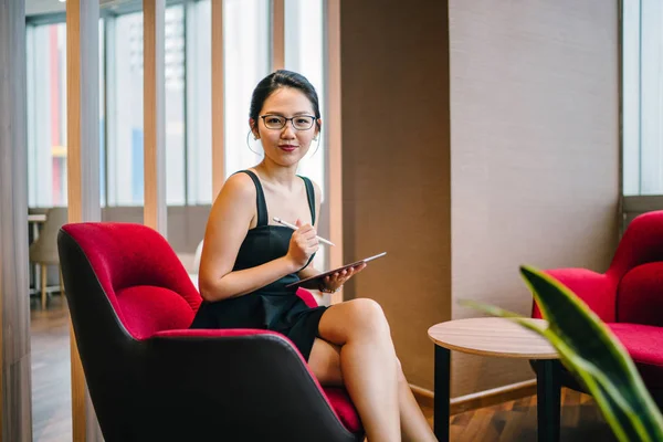一位年轻貌美的亚洲女人坐在同事的办公室里 用一支笔在平板电脑上工作 她的商业肖像 — 图库照片