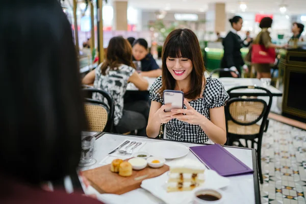 A Chinese Asian lady enjoys high tea with a good friend at a restaurant. She is beautiful, elegant and is smiling as she talks animatedly with her friend over cakes and tea on a weekend.