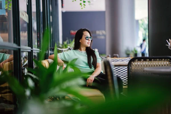 Genç ve çekici Çinli Asyalı bir kadının portresi uzanarak ve bir hafta sonu gün boyunca bir kafede rahatlatıcı. Nane yeşili bir kazak giyiyor.
