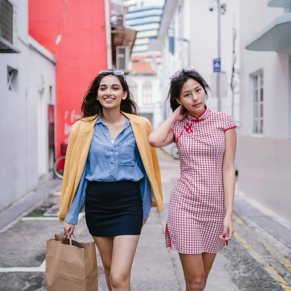 iki yakın arkadaş birlikte bir ara Sokaktan yürürken. Onlar birlikte mutlu bir şekilde yürürken onlar hem trendy retro giyim ve tutuşup giyiyorsun. Çince, diğer Hint biri