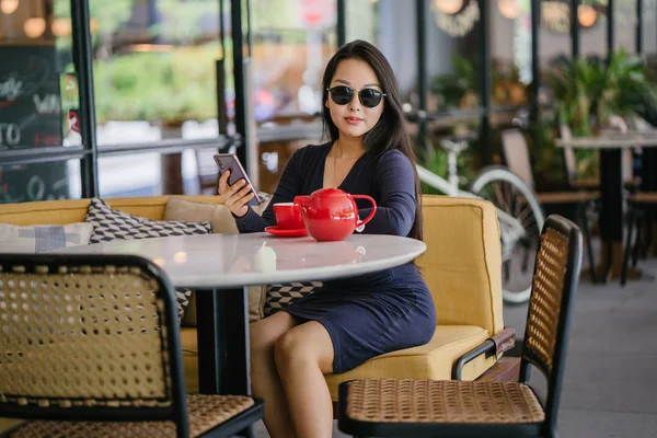 Bir açık havada açık havada oturan ve kırmızı bir çay seti çay sıcak bir fincan zevk genç, çekici, zarif ve güzel Asyalı kadın Portresi. 