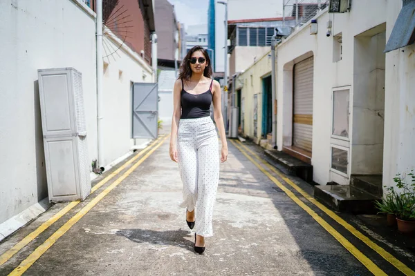 Genç, uzun boylu, ince ve zarif Hint Asyalı kadın rahat bir kıyafet içinde Asya bir sokakta bir sokakta aşağı gün boyunca yürür