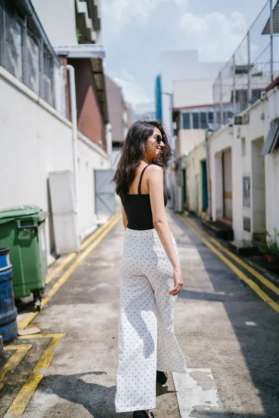 Genç, uzun boylu, ince ve zarif Hint Asyalı kadın rahat bir kıyafet içinde Asya bir sokakta bir sokakta aşağı gün boyunca yürür