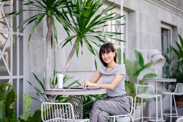 Açık havada şık bir yerde oturan bir emin, şık ve çekici orta yaşlı Çinli Asyalı kadın portresi. O bir pohpohlama gri kıyafeti giyiyor.