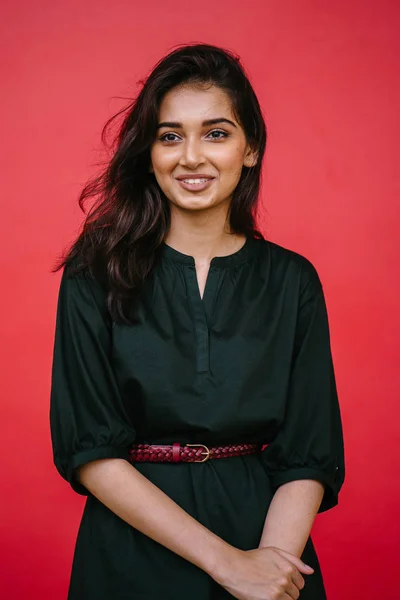 スタジオの赤いスタジオを背景に美しい 魅力的なインド アジアの女性の肖像画 彼女はシンプルな緑のドレスと赤帯のエレガントな服を着て 笑顔です — ストック写真