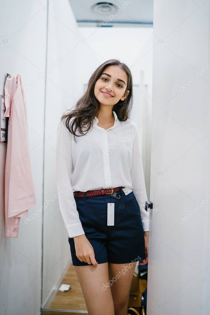 Portrait of a young, tall, beautiful and elegant Indian Asian woman trying out clothing in a fitting room at a fashion store.