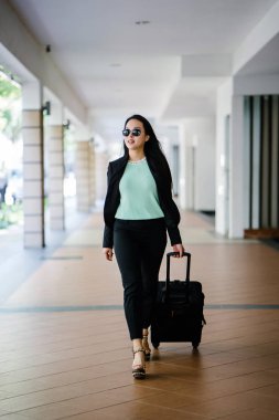 Genç bir Asyalı kadın bavulunu çekiyor. O çekici, zarif ve şık giyinmiş