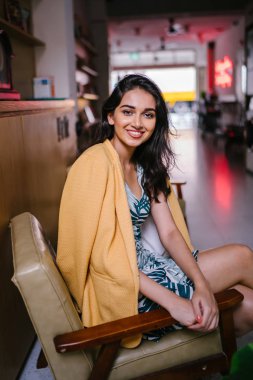 güzel, genç ve şık Hint Asyalı kadın manifatura onun Smartphone olarak o gün karşı bir çıkıntıya doğru eğilir. O rahat kıyafetler üzerinde bir retro sarı ceket giyiyor