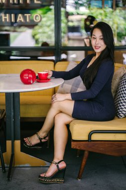 Bir açık havada açık havada oturan ve kırmızı bir çay seti çay sıcak bir fincan zevk genç, çekici, zarif ve güzel Asyalı kadın Portresi. 