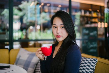 Bir açık havada açık havada oturan ve kırmızı bir çay seti çay sıcak bir fincan zevk genç, çekici, zarif ve güzel Asyalı kadın Portresi. 