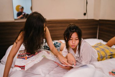 İki genç Asyalı arkadaş bir pansiyonda bir yatakta oturuyor. İkisi de Asyalı ve birlikte seyahat ediyorlar. Biri Hintli, diğeri Çinli. İkisi de gündelik giysiler içinde ve odalarında dinleniyorlar..