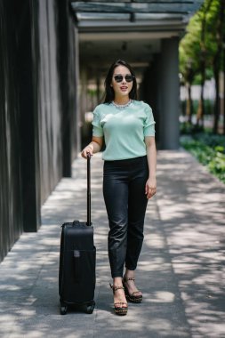 Genç bir Asyalı kadın bavulunu çekiyor. O çekici, zarif ve şık giyinmiş