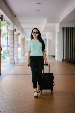 Genç bir Asyalı kadın bavulunu çekiyor. O çekici, zarif ve şık giyinmiş
