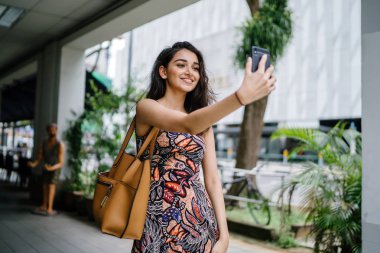 Genç, güzel ve zarif Punjabi Hint Asyalı kadın kendini bir selfie onun smartphone ile yoğun bir cadde üzerinde gün boyunca alır