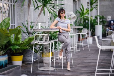 Açık havada şık bir yerde oturan bir emin, şık ve çekici orta yaşlı Çinli Asyalı kadın portresi. O bir pohpohlama gri kıyafeti giyiyor.