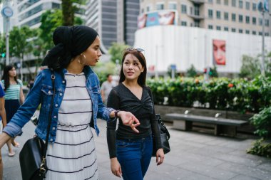 İki arkadaş, Orchard Road, Singapur, Asya 'da aydınlık bir yaz gününde mutlu bir şekilde yürüyüp konuşurlar. Biri Müslüman Malezyalı, diğeri Çinli bir kadın.. 