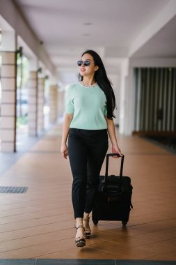 Genç bir Asyalı kadın bavulunu çekiyor. O çekici, zarif ve şık giyinmiş