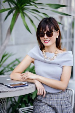 Açık havada şık bir yerde oturan bir emin, şık ve çekici orta yaşlı Çinli Asyalı kadın portresi. O bir pohpohlama gri kıyafeti giyiyor.