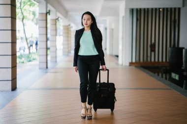 Genç bir Asyalı kadın bavulunu çekiyor. O çekici, zarif ve şık giyinmiş