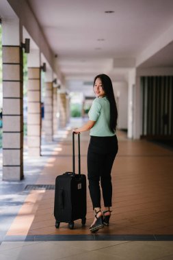 Genç bir Asyalı kadın bavulunu çekiyor. O çekici, zarif ve şık giyinmiş