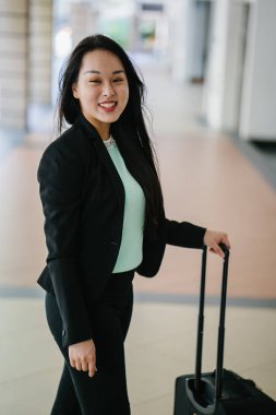 Genç bir Asyalı kadın bavulunu çekiyor. O çekici, zarif ve şık giyinmiş