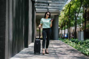 Genç bir Asyalı kadın bavulunu çekiyor. O çekici, zarif ve şık giyinmiş