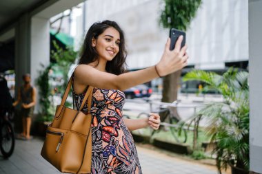 Genç, güzel ve zarif Punjabi Hint Asyalı kadın kendini bir selfie onun smartphone ile yoğun bir cadde üzerinde gün boyunca alır