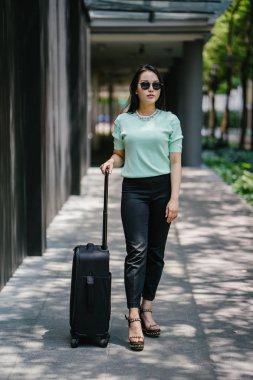 Genç bir Asyalı kadın bavulunu çekiyor. O çekici, zarif ve şık giyinmiş