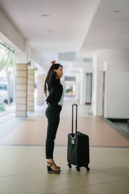 Genç bir Asyalı kadın bavulunu çekiyor. O çekici, zarif ve şık giyinmiş