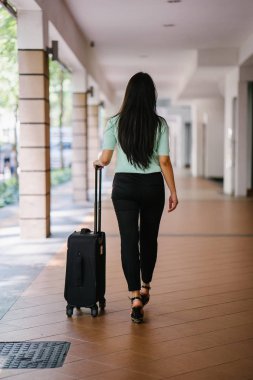 Genç bir Asyalı kadın bavulunu çekiyor. O çekici, zarif ve şık giyinmiş