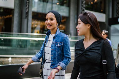 İki arkadaş, Orchard Road, Singapur, Asya 'da aydınlık bir yaz gününde mutlu bir şekilde yürüyüp konuşurlar. Biri Müslüman Malezyalı, diğeri Çinli bir kadın.. 