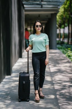 Genç bir Asyalı kadın bavulunu çekiyor. O çekici, zarif ve şık giyinmiş