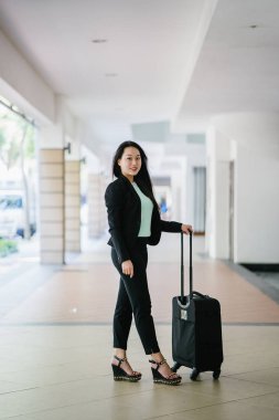 Genç bir Asyalı kadın bavulunu çekiyor. O çekici, zarif ve şık giyinmiş