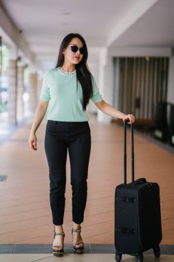 Genç bir Asyalı kadın bavulunu çekiyor. O çekici, zarif ve şık giyinmiş