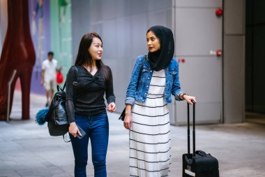 İki arkadaş, Orchard Road, Singapur, Asya 'da aydınlık bir yaz gününde mutlu bir şekilde yürüyüp konuşurlar. Biri Müslüman Malezyalı, diğeri Çinli bir kadın.. 