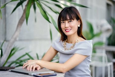 Açık havada şık bir yerde oturan bir emin, şık ve çekici orta yaşlı Çinli Asyalı kadın portresi. O bir pohpohlama gri kıyafeti giyiyor.