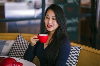 Bir açık havada açık havada oturan ve kırmızı bir çay seti çay sıcak bir fincan zevk genç, çekici, zarif ve güzel Asyalı kadın Portresi. 