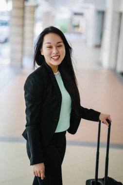 Genç bir Asyalı kadın bavulunu çekiyor. O çekici, zarif ve şık giyinmiş