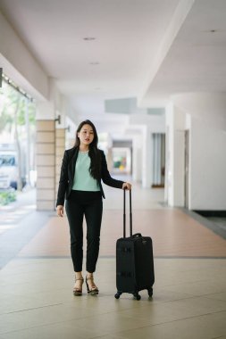 Genç bir Asyalı kadın bavulunu çekiyor. O çekici, zarif ve şık giyinmiş