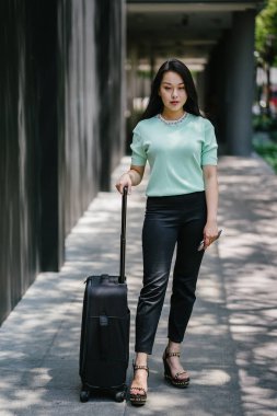 Genç bir Asyalı kadın bavulunu çekiyor. O çekici, zarif ve şık giyinmiş
